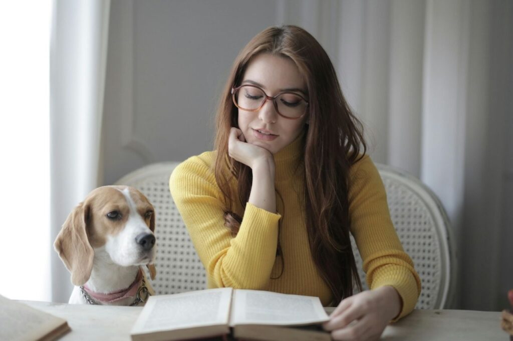 A woman reading an English grammar reference books with her dog beside her, showing relaxed and enjoyable English learning at home.