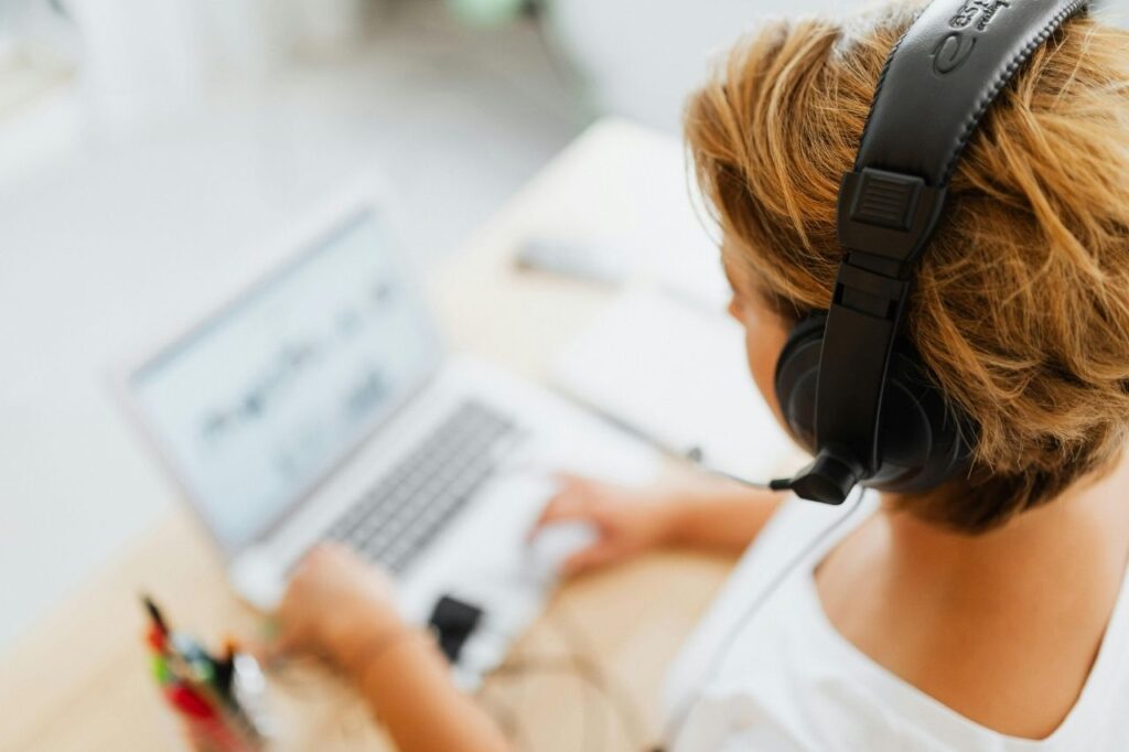 A person using a laptop with large headphones, studying through an AI-powered English learning platform.