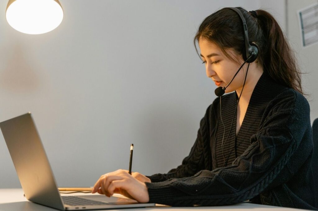 A woman smiling while learning English online using one of the best English learning apps on her laptop.
