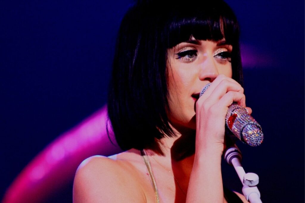 Katy Perry singing live during a concert with a sparkling crystal microphone under soft stage lighting for her biography feature