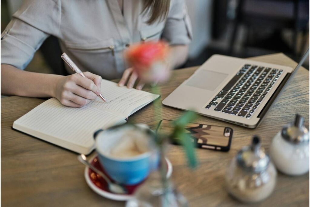 A person writing in a notebook next to a laptop during English writing practice.